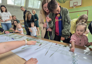 dzieci i rodzice przyklejają do kartonu trawy i kwiaty