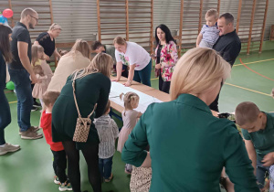 dzieci wraz z rodzicami tworzą pracę plastyczną przyklejają do kartonu trawy i kwiaty
