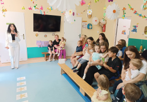 rodzice z dziećmi siedzą na ławkach, słuchają przemówienia pani dyrektor