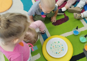 dzieci siedzą na dywanie przyglądają się kropkom a talerzyku
