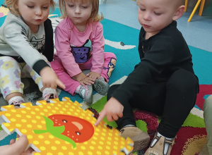 dzieci siedzą na dywanie i pokazują palcem kropki na obrazku