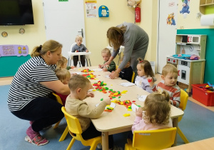 opiekunki pomagają dzieciom w klejeniu bibuły