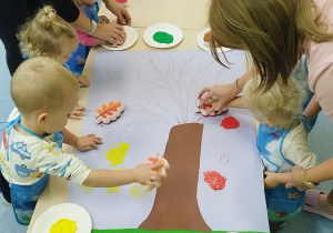 opiekunki pomagają dzieciom stemplować liście na kartonie z narysowanym drzewem
