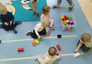 dzieci siedzą na podłodze i układają na liniach klocki