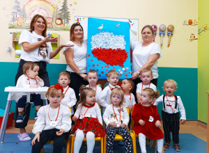 żlobkowe dzieci i opiekunki pozują do zdjęcia trzymając wspólnie wykonaną pracę plastyczną