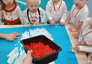 opiekunka rozdaje dzieciom czerwoną bibułe