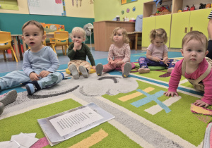 dzieci siedzą na dywanie, słuchają opiekunki