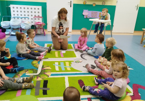 dzieci siedząc na dywanie słuchają czytanego przez opiekunkę wiersza