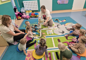 opiekunka pokazuje dzieciom siedzącym na dywanie ilustrację z opowiadania o misiu