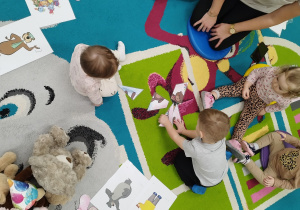 dzieci siedzą na dywanie próbują ułożyć puzzle