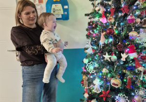 opiekunka trzyma na rękach dziecko, dziecko uśmiecha się na widok choinki