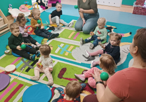dzieci z opiekunkami siedzą na dywanie i grają na instrumentach