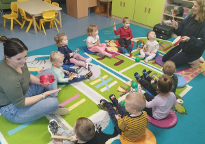 dzieci i opiekunki siedzą na dywanie i grają na instrumentach