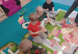dzieci i opiekunka układają rozsypane obrazki na dywanie