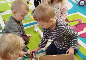 dzieci zbierają z dywanu kulki przy pomocy pęset