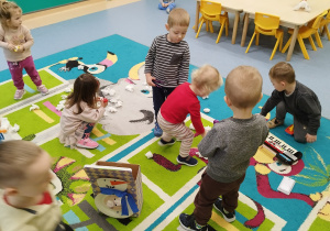 na dywanie rozsypane papierowe kule, dzieci zbierają je za pomocą pęset