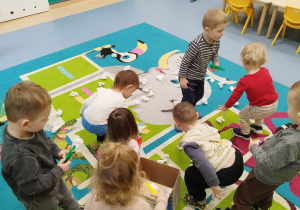 dzieci trzymają w rękach pęsety, na dywanie leżą rozsypane kulki papierowe