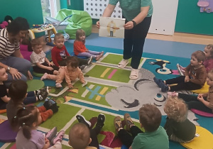 opiekunka pokazuje dzieciom siedzącym na dywanie ilustrację, przedstawiającą piekarza