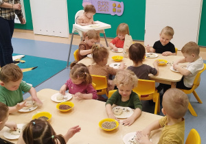 dzieci przy stoliku ugniatają ciasto u wkładają pestki, które mają w miseczkach na stole