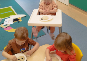 dzieci wbijają pestki w ciasto, dziewczynka w krzesełku uśmiecha się