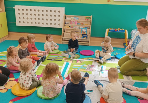 opiekunki wraz z dziećmi siedzą na dywanie , opiekunka pokazuje ilustracje