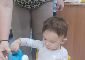 opiekunka pomaga chłopcu podlać konewką rzeżuchę