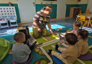dzieci siedzą na dywanie , opiekunka pokazuje palemkę