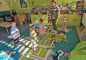 dzieci i opiekunka stoją na dywanie- zabawa ruchowa