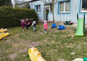 opiekunka trzyma wiaderko, dzieci noszą jajka na łyżkach