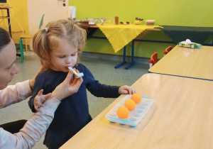 mama trzyma dziewczynce papierowy gwizdek, przed nią leżą piłeczki ping-pongowe