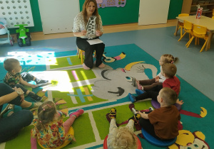 dzieci siedzą na dywanie, opiekunka pokazuje im pingwina