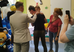 chłopiec trzymany przez tatę podaje rękę panu burmistrzowi, mama stoi i sie uśmiecha