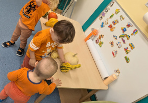 chłopiec unosi dynię wysoko, a dwóch chłopców ogląda te leżące na stoliku