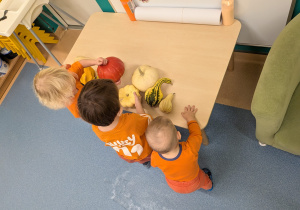 dzieci stoją przy stoliku, na którym leżą różne dynie