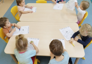 dzieci siedzą przy stoliku , kolorują malowankę