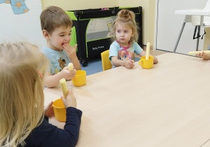 dzieci siedzą przy stoliku , trzymaja chrupkę i kubek z miodem