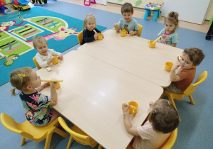 dzieci siedzą przy stoliku jedzą chrupki maczając je w kubku z miodem