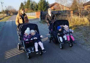 dwie opiekunki pchają wózki z siedzącymi w nich dziećmi