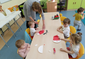 dzieci siedzą przy stoliku, niektóre robią pracę plastyczną