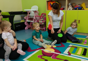 dzieci siedzą z opiekunkami na dywanie