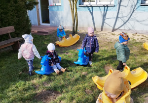 dzieci chodzą po trawie, siedzą i wsiadają na bujaki