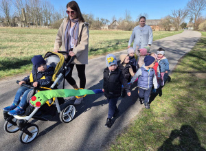opiekunka pcha wózek za nią maszerują dzieci wraz z opiekunką