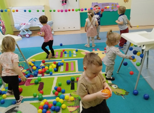 na podłodze dużo kolorowych piłek, dzieci je zbierają