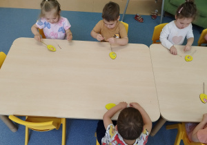 dzieci przy stoliku przyklejają ozdoby do jajka