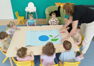 dzieci siedzą przy stoliku, na którym leży karton i elementy planety