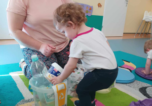 dziewczynka wrzuca do wiaderka śmieć, a opiekunka patrzy