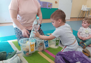 chłopiec wrzuca do odpowiedniego wiaderka plastikową butelkę