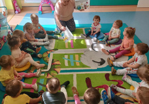 dzieci siedzą na dywanie , opiekunka pokazuje plansze