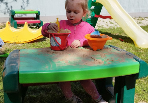dziewczynka siedzi przy stoliku i bawi się zabawkami z piasekim