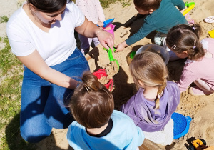 opiekunka z grupką dzieci robią babki w piaskownicy